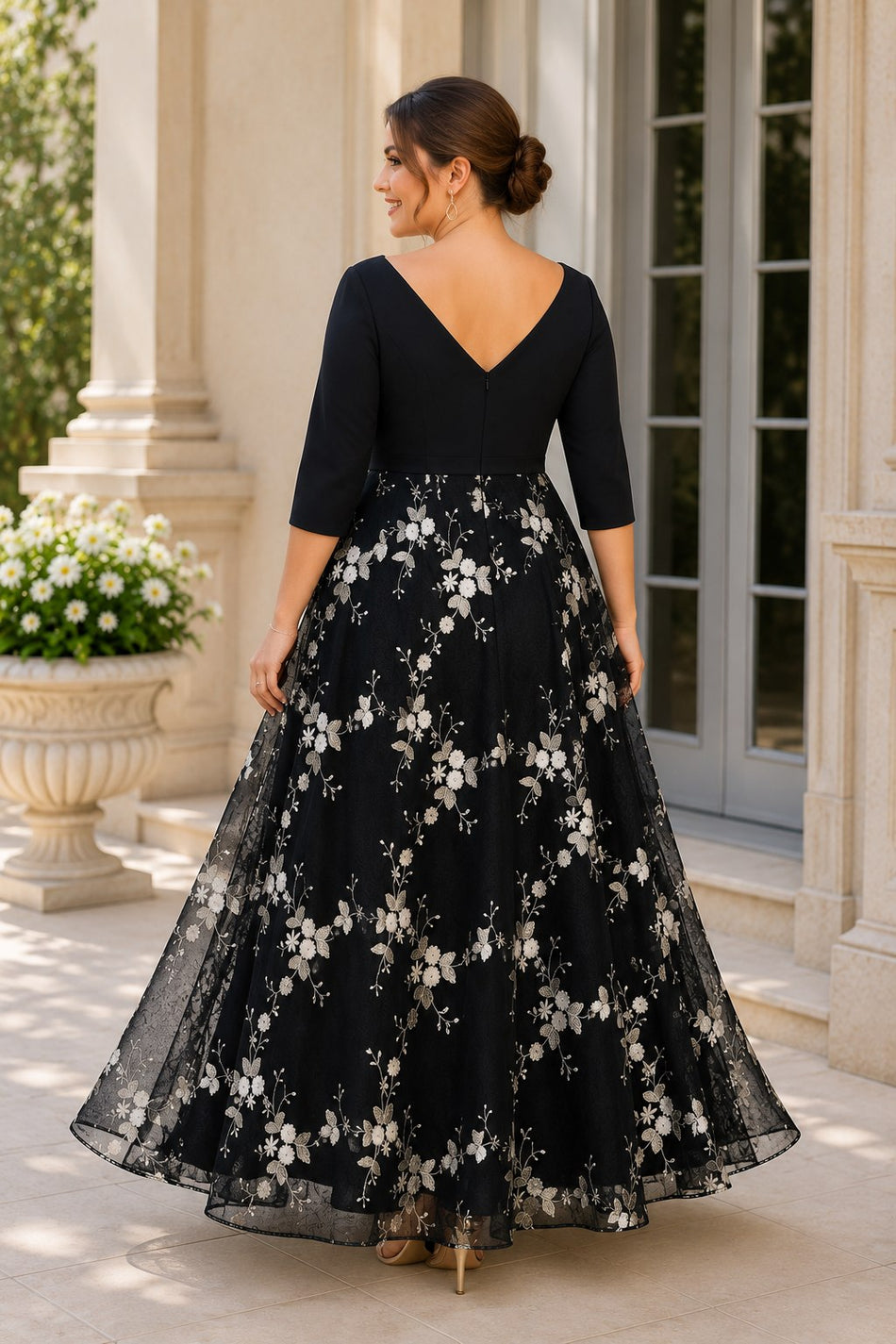 Back view of a plus size black formal dress featuring a V-back neckline, three-quarter sleeves and a floral embroidered full-length A-line skirt.
