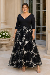 Front view of a plus size black formal dress with three-quarter sleeves, V-neckline and floral embroidered A-line skirt.