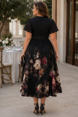 Elegant back view of plus size black floral midi dress with flutter sleeves, wrap neckline and flowing skirt. Perfect for weddings, parties and special occasions.