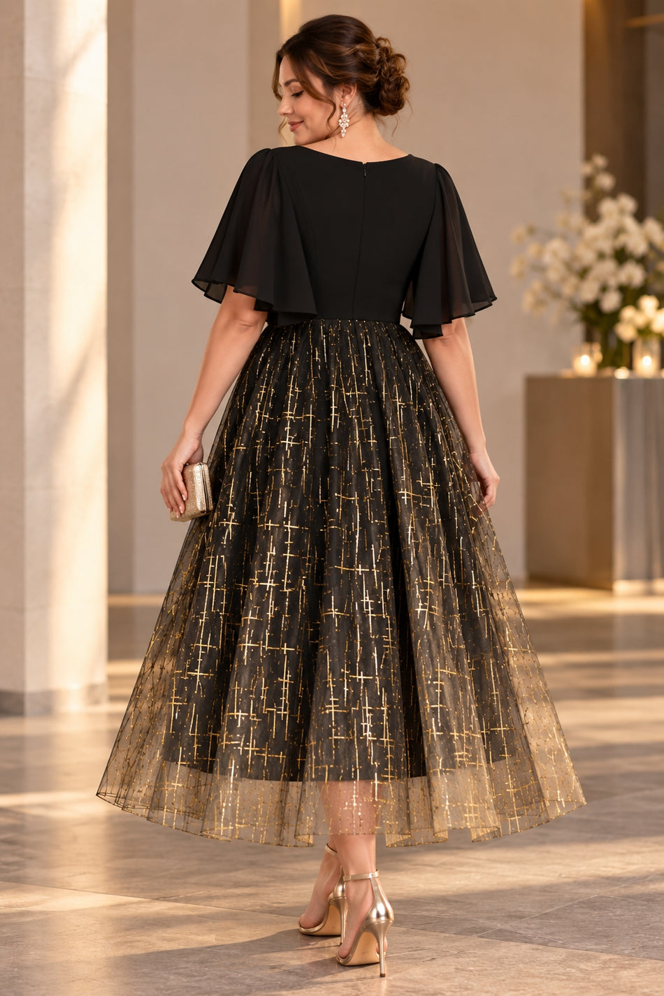 Back view of a plus size black and gold midi cocktail dress with flutter sleeves and a full metallic patterned skirt.