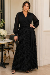 Plus size woman wearing a black evening maxi dress with wrap-style V-neck, long sheer sleeves, defined waist and textured A-line skirt.