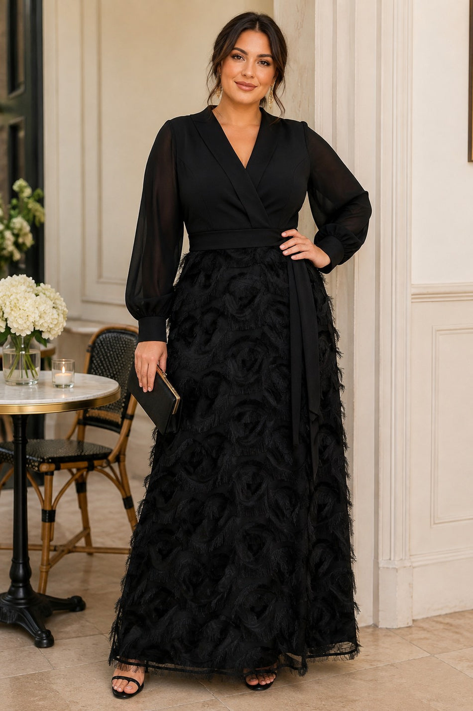 Plus size woman wearing a black evening maxi dress with wrap-style V-neck, long sheer sleeves, defined waist and textured A-line skirt.
