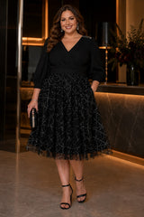 Plus size woman wearing a black midi cocktail dress with V neckline, three-quarter sleeves, defined waist and sparkling full skirt.