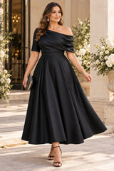 Plus size woman wearing a black satin midi formal dress with an asymmetric off-shoulder neckline and flowing A-line skirt.