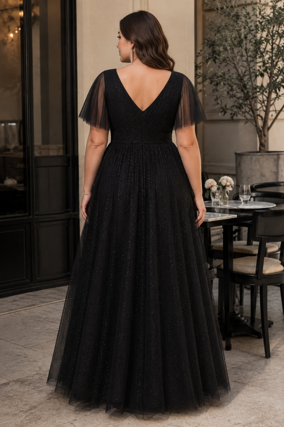 Back view of a plus size black sparkle formal dress with elegant V-back, flutter sleeves and flowing full-length skirt.