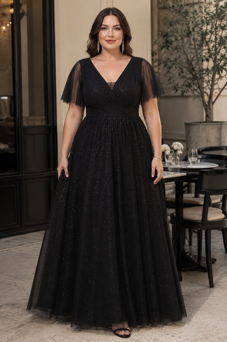 Front view of a plus size black sparkle formal dress with draped V-neck bodice, flutter sleeves and flowing floor-length skirt.