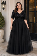 Plus size woman wearing a black floor-length A-line formal dress with sequin V-neck bodice, short sleeves and full tulle skirt.
