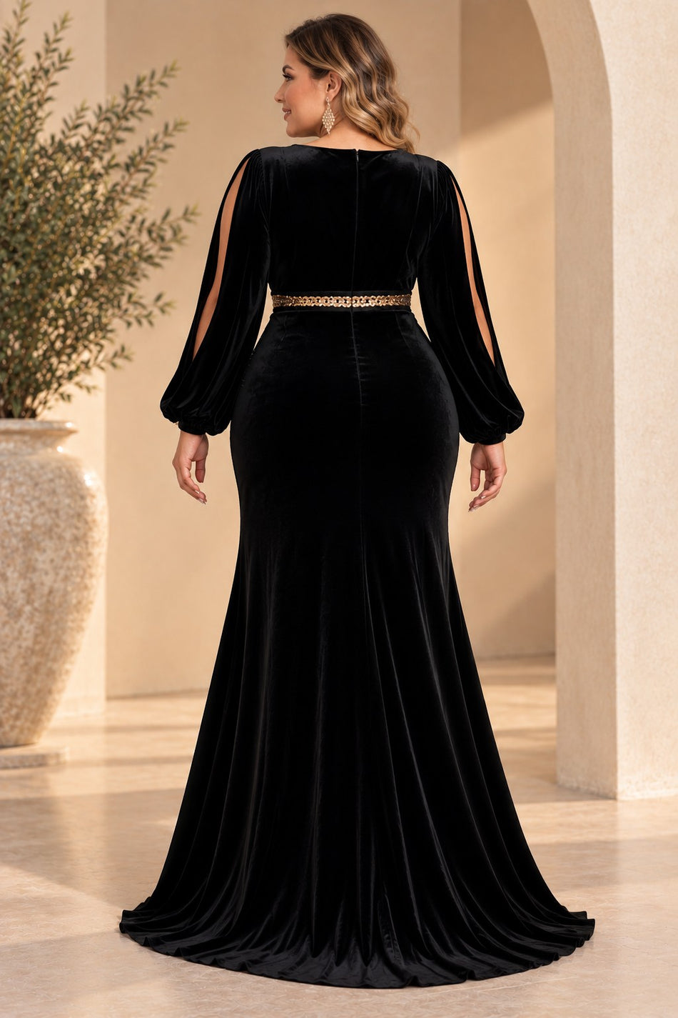 Back view of a plus size woman wearing a black velvet evening dress with long split sleeves, defined gold-toned waist and flared floor-length skirt.