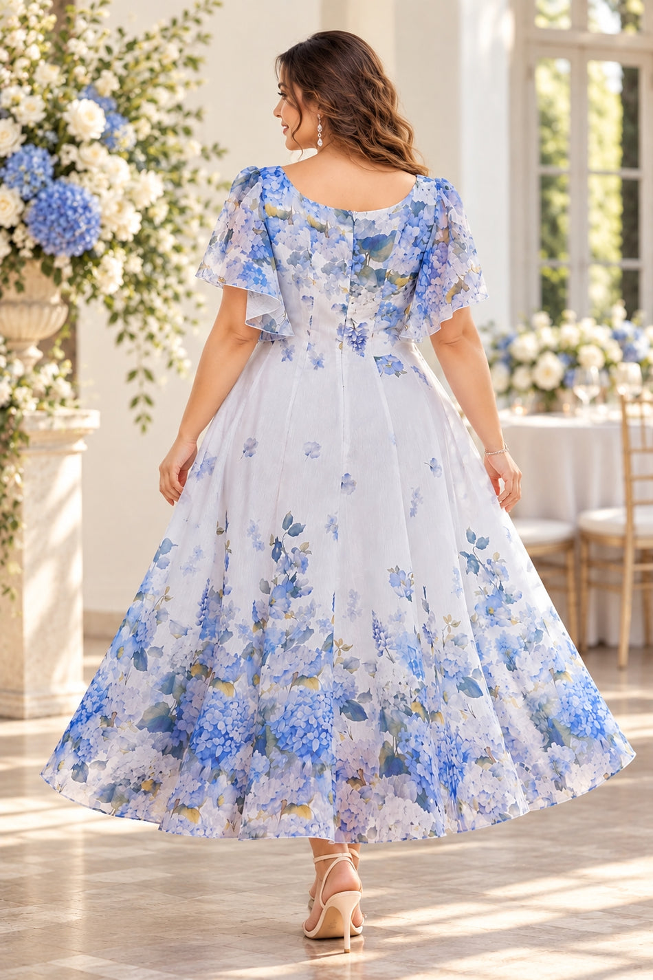 Back view of a blue floral wedding guest dress with flutter sleeves, fitted waist and flowing A-line skirt.