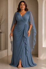 Plus size woman wearing a blue wrap maxi formal dress with V-neckline, flowing cape sleeves and cascading front drape.
