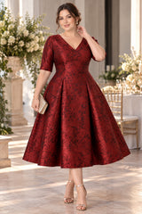 Plus size woman wearing a burgundy floral jacquard midi wedding guest dress with V-neckline, elbow sleeves and full flared skirt, front view.
