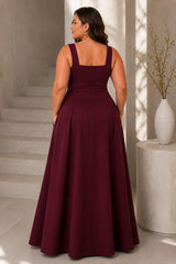Back view of a plus size woman wearing a burgundy formal maxi dress with wide straps, square back neckline and full A-line skirt.