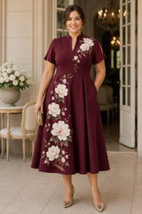 Front view of a plus size burgundy Oriental-inspired wedding guest dress featuring a mandarin collar, peony floral print, short sleeves and flowing A-line midi skirt.