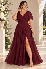 Plus size woman wearing a burgundy wrap-style maxi formal dress with V neckline, flutter sleeves and cascading front drape.