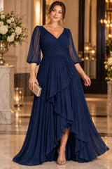Plus size woman wearing a navy maxi evening dress with pleated V-neck bodice, sheer three-quarter sleeves and cascading front skirt.
