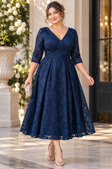 Woman wearing a navy blue floral lace wedding guest midi dress with V-neckline, three-quarter sleeves and pleated A-line skirt.