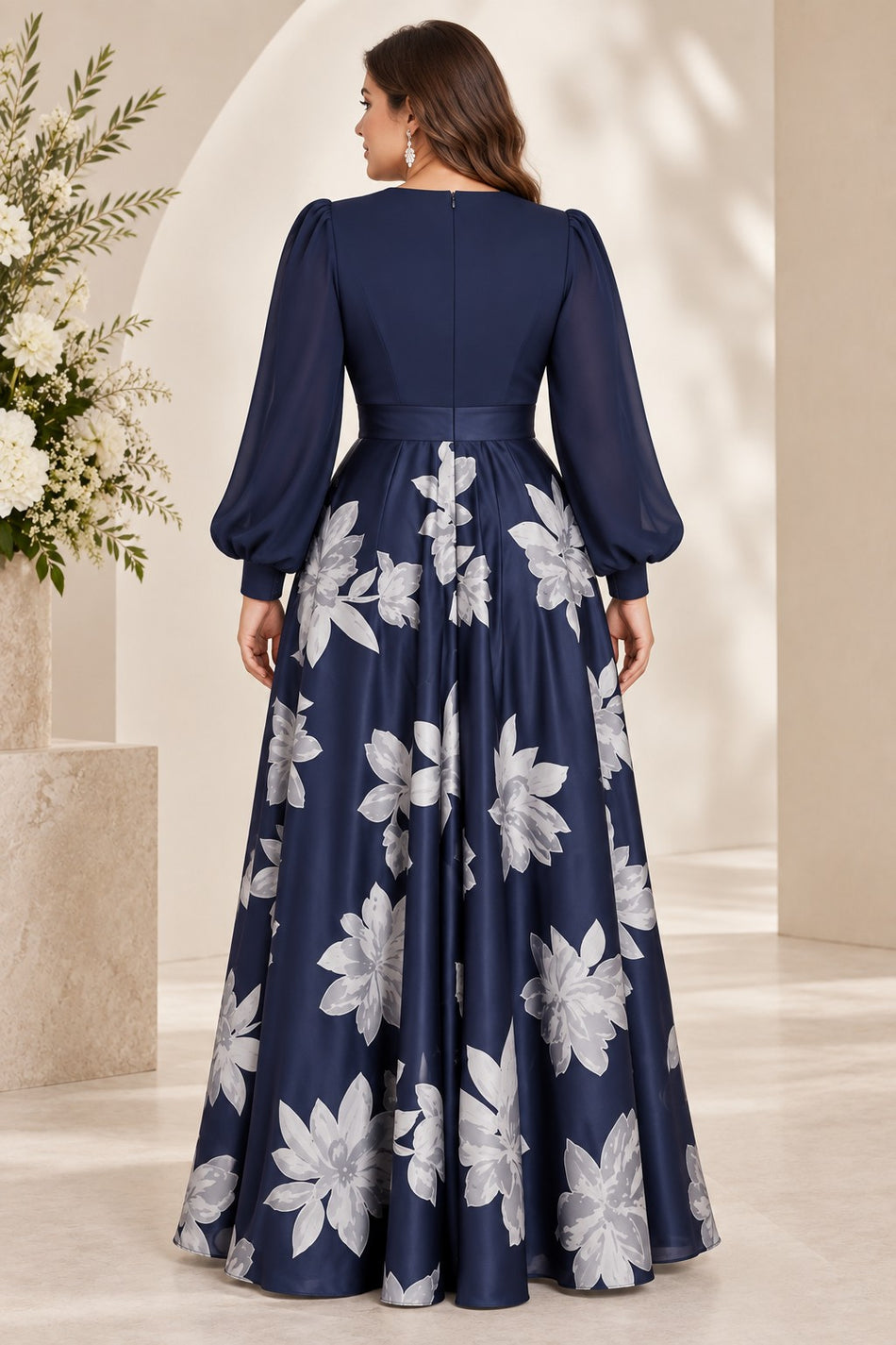 Back view of a plus size navy evening dress with long sleeves, defined waistband and full silver-white floral floor-length skirt.