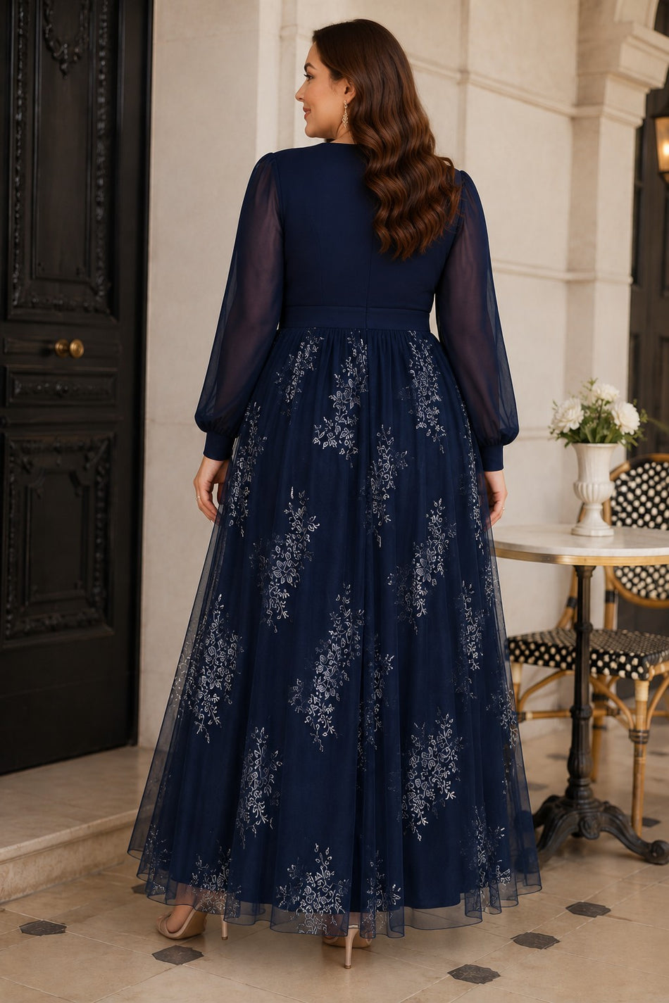 Back view of a plus size navy floral evening dress with sheer long sleeves, defined waistband and flowing full-length skirt.