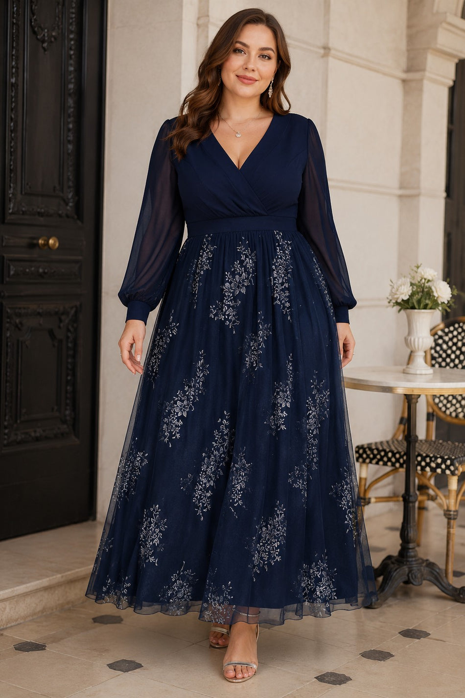 Plus size woman wearing a navy floral evening dress with wrap V-neck bodice, sheer long sleeves, defined waist and flowing maxi skirt.