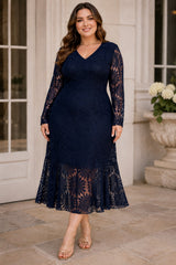 Plus size woman wearing a navy lace wedding guest dress with V-neckline, long sheer lace sleeves and flared hem.
