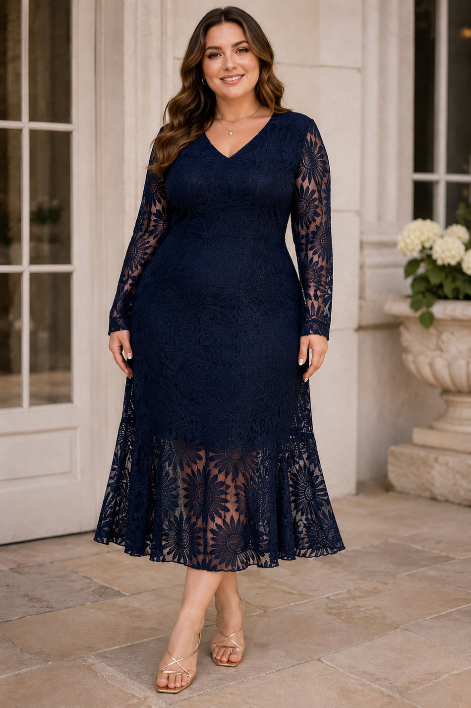 Plus size woman wearing a navy lace wedding guest dress with V-neckline, long sheer lace sleeves and flared hem.