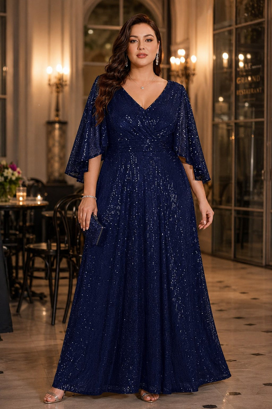 Plus size woman wearing a navy sequin maxi evening dress with flutter sleeves, V-neckline and flowing full-length skirt.