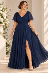 Plus size woman wearing a navy wrap-style maxi formal dress with V neckline, flutter sleeves and cascading front drape.