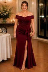 Plus size woman wearing a burgundy off shoulder evening gown with a draped waist, front split and full-length fit-and-flare silhouette.