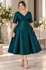 Plus size woman wearing a deep teal floral jacquard midi dress with V-neckline, elbow sleeves and full A-line skirt, front view.