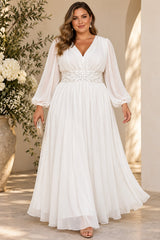 Plus size woman wearing a white V-neck maxi dress with sheer long sleeves, embellished waist and flowing full-length skirt.